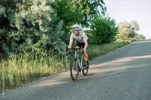 Male professional sportsman cyclist training on a road bike outside the city on an asphalt road, riding downhill © bodnarphoto