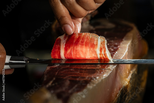 Slice of Iberian ham from Spain 100% acorn-fed, cut with a knife by a professional. Close up view of ham cutter typical of Spain gourmet product for international sale, selective focus