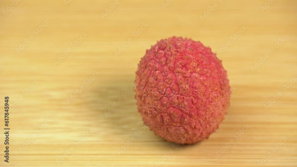 Fresh lychee fruit in shell rotate in macro on wooden background. Lychee berries for making lemonade and refreshing drink Fresh lychee fruit in shell rotate in macro on wooden background. Lychee berries for making lemonade and refreshing drink