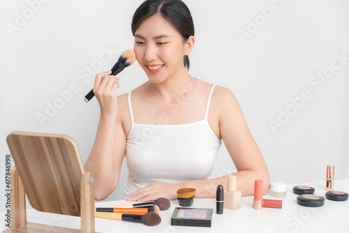 An Asian beauty blogger uses a blush brush to brush on her face during a live online makeup tutorial via the Internet.