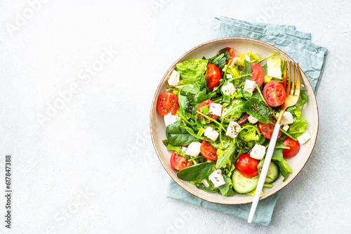 Green salad with spinach, arugula, tomatoes and feta with olive oil. Top view on white.