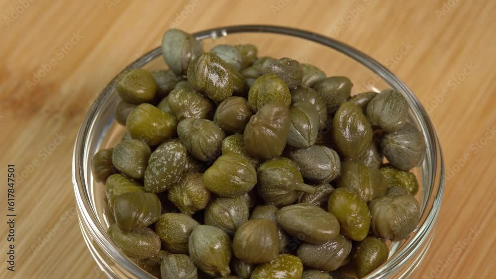 Pickled marinated capers rotate in glass bowl in macro. Ingredients for making spicy sauce, tartare or salad Pickled marinated capers rotate in glass bowl in macro. Ingredients for making spicy sauce, tartare or salad