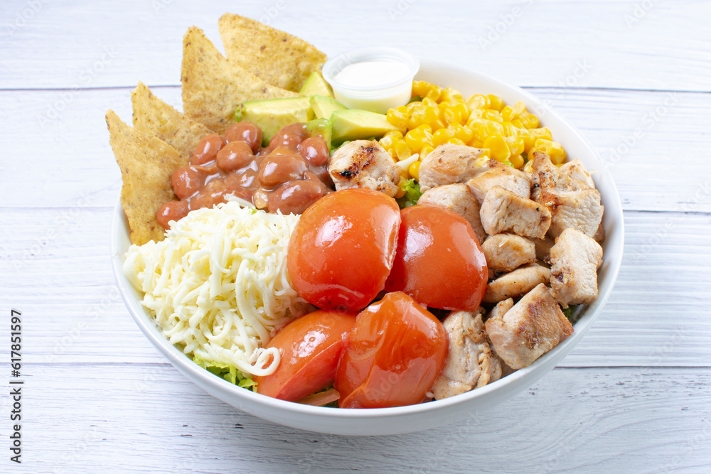 Bowl salad with pieces of roasted pork, grated cheese, beans, corn, tomato, nachos, lettuce, with house mayonnaise