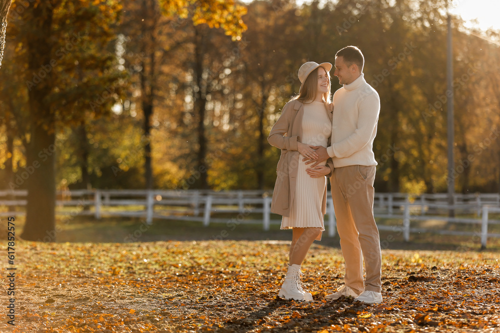Fototapeta premium Young stylish couple lovers are hugging and kissing in the autumn park. Lovely romantic moment between man and woman in love, looking to each others. Happy family. Love, youth, happiness concept.
