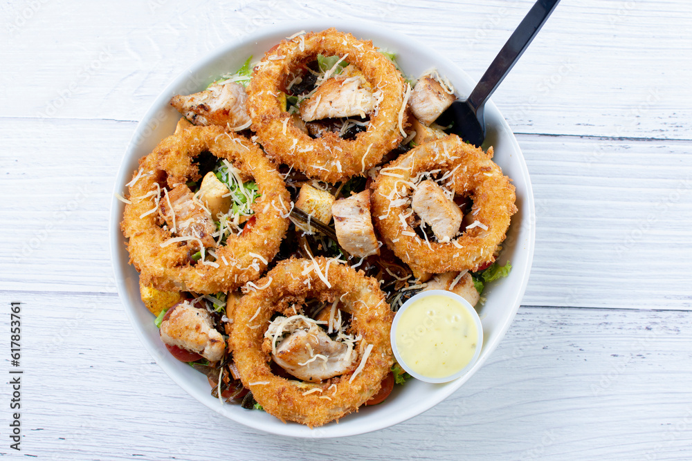 Bowl salad with pieces of roast pork, grated cheese, onion rings and house mayonnaise