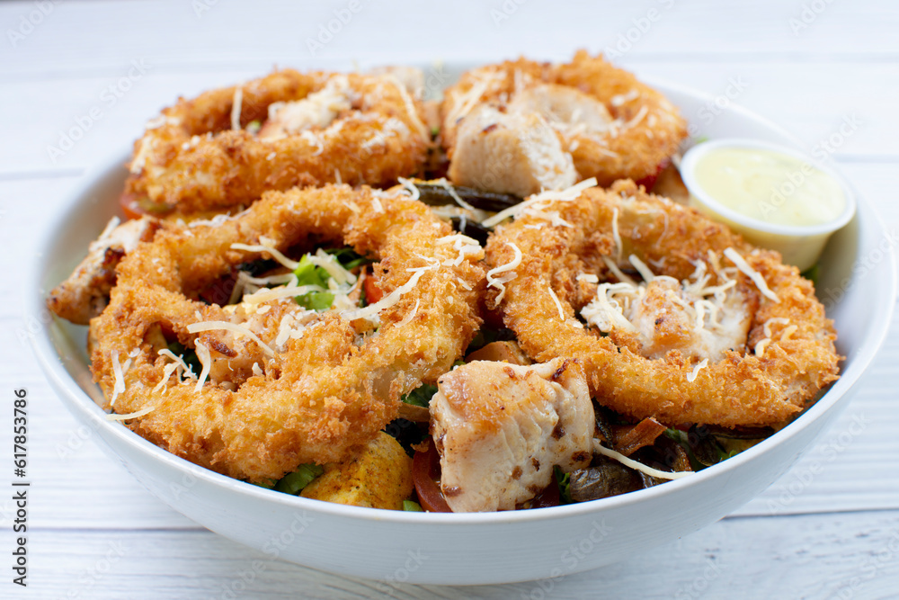 Bowl salad with pieces of roast pork, grated cheese, onion rings and house mayonnaise