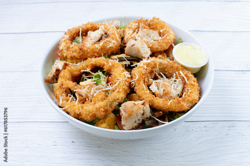 Bowl salad with pieces of roast pork, grated cheese, onion rings and house mayonnaise