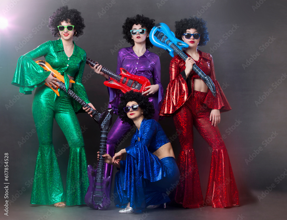 Girls in bright shiny costumes and wigs with guitars. Vintage music disco band for women in disco style.