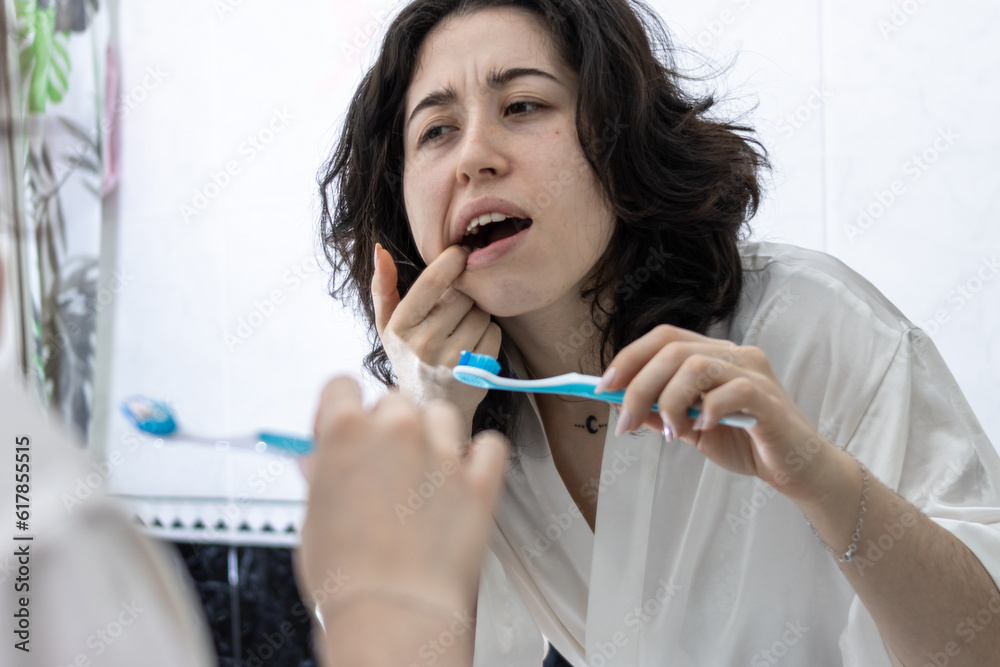 young latin woman looking at mirror while suffering from tooth pain young latin woman looking at mirror while suffering from tooth pain