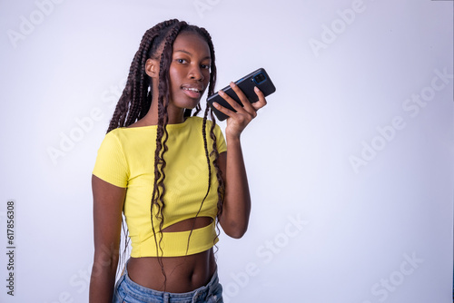 Mujer hermosa joven de color que usa el teléfono inteligente  en una fondo blanco. Chica estudiante sonriente enviando mensajes de voz en el teléfono móvil.. photo