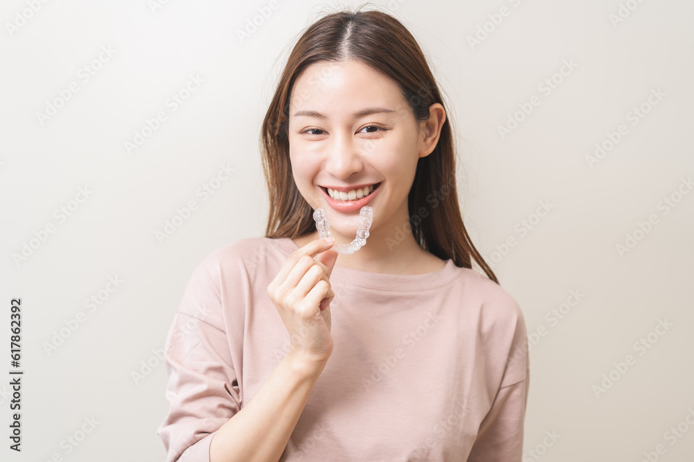 Dental invisible braces, beautiful smiling asian young woman holding invisalign braces, wearing orthodontic silicone trainer, white smile using invisible whitening tray. Stomatology, dental healthcare Dental invisible braces, beautiful smiling asian young woman holding invisalign braces, wearing orthodontic silicone trainer, white smile using invisible whitening tray. Stomatology, dental healthcare