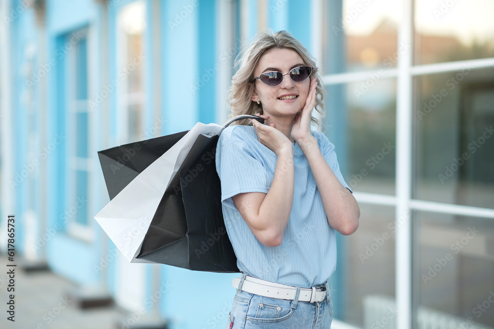 Fototapeta premium A young girl in a blue sweater and sunglasses surprised joyful. With shopping bags.