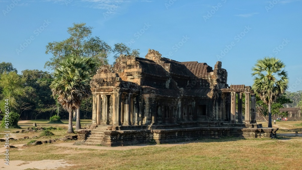 Photograph of a weathered stone building from the Khmer Empire in Southeast Asia under the sun, symbol of ancient Cambodian architecture.