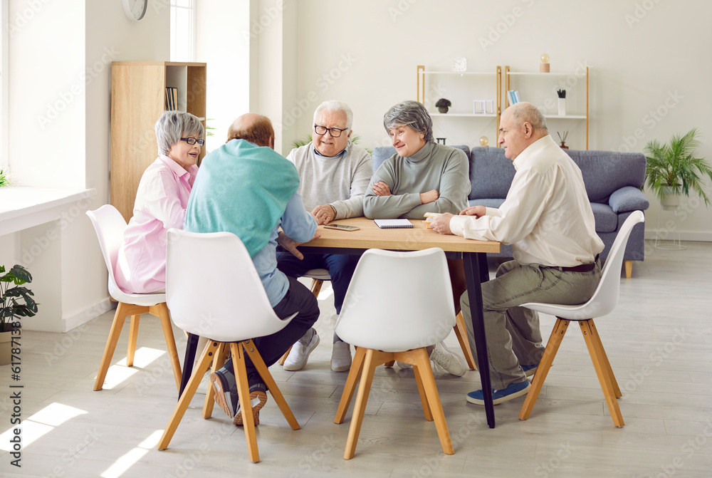 Senior people spending time in retirement home. Group of old male and female friends sitting around table, playing dominoes, taking turns to draw pieces, thinking of strategy and enjoying leisure time