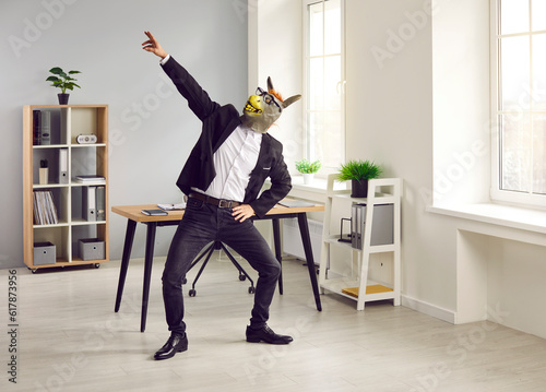 Man in suit and funny animal mask having fun at end of work day. Happy lazy irresponsible guy dancing in office wearing unusual bizarre silly wacky rubber donkey mask in glasses. Weekend party concept
