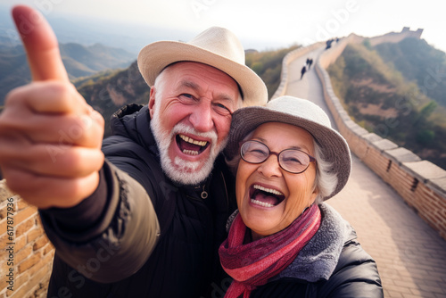 A happy elderly tourist couple take a selfie in China with the Great Wall in the background. Travel retirement concept. AI generated. © serperm73