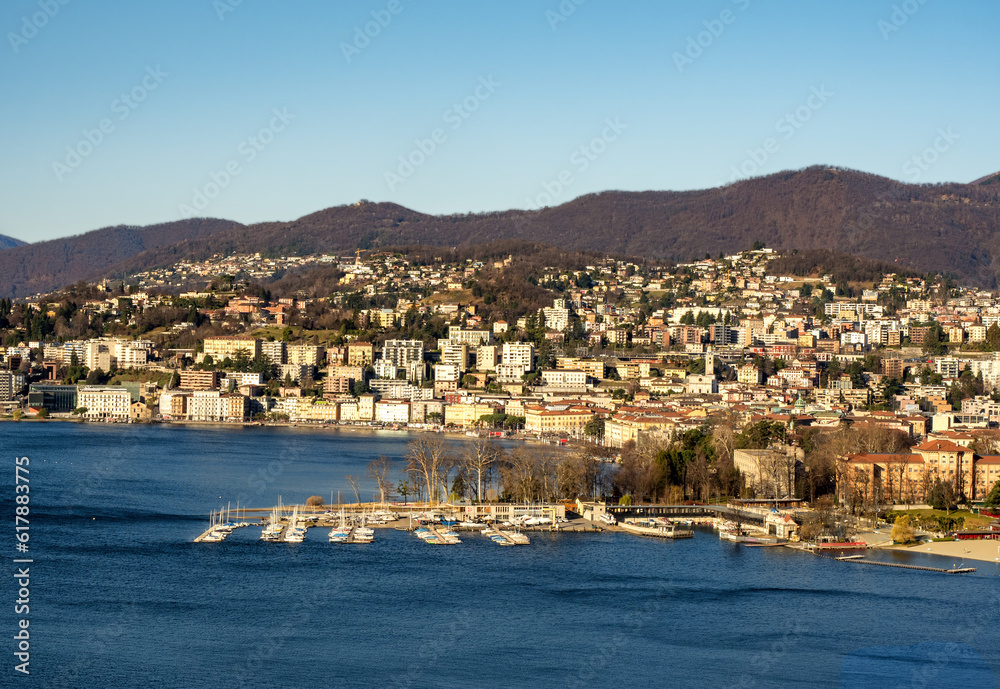 panorama in the morning of Lake Lugano, with the lake intensely blue in color, on its shore the city of Lugano, on the right a marina