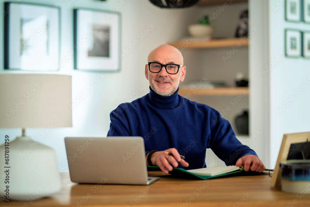 Smiling mid aged businessman sitting at home and using computer for work Smiling mid aged businessman sitting at home and using computer for work