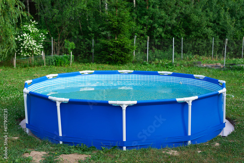 Blue portable country pool on the lawn of a country garden.