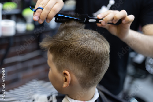 Beautiful child in a barber chair on a haircut. A child boy sits calmly in a chair while a professional hairdresser cuts his hair. The concept of a child in a barbershop.