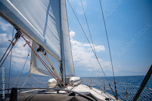 Yacht sailing in an open sea. Close-up view of the deck  mast and sails. Clear sky  waves and water splashes