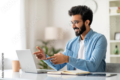 Teleconference. Smiling Indian Freelancer Guy Making Video Call With Laptop At Home