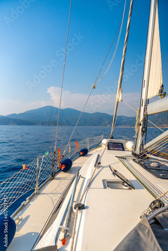 Yacht sailing in an open sea. Close-up view of the deck, mast and sails. Clear sky, waves and water splashes © dtatiana