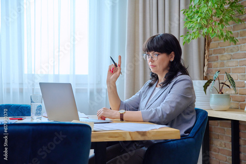 Mature business woman at workplace using laptop for virtual video meeting photo