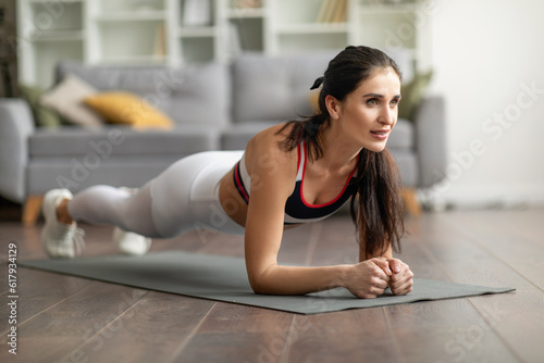 Beautiful athletic young lady planking on fitness mat at home