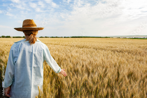 Obraz na płótnie A young woman in a straw hat walks in a wheat field. Back view. w salonie