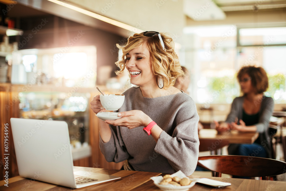 Young woman having a cup of coffee in a cafe while using a laptop