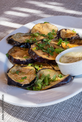 Plateful of Fried Sliced Aubergine or Eggplant Covered with Fresh Flat Leaf Parsley and Served with Pureed Roasted Garlic