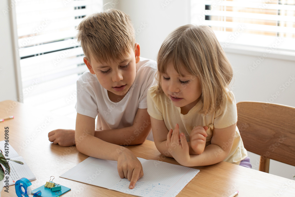 The older brother teaches the younger sister to read letters. Brother and sister, home schooling.