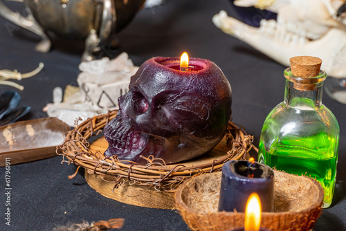 Human skull candle selective focus, arranged with black candles and spell potion vials on witchcraft background. Magic tools and items. Occult and esoteric concept. Magic chemistry and witch craft.