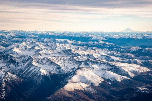View of the snow covered Andes mountains and volcanoes through the window of an airplane at sunrise