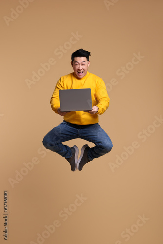 Happy man with laptop jumping on beige background © New Africa