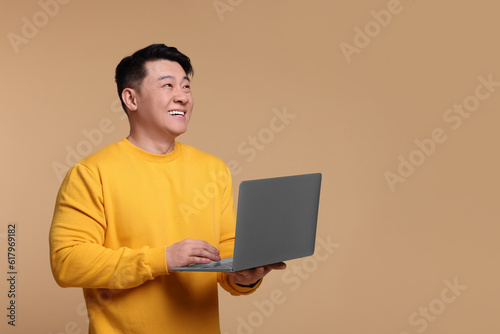 Happy man with laptop on beige background, space for text