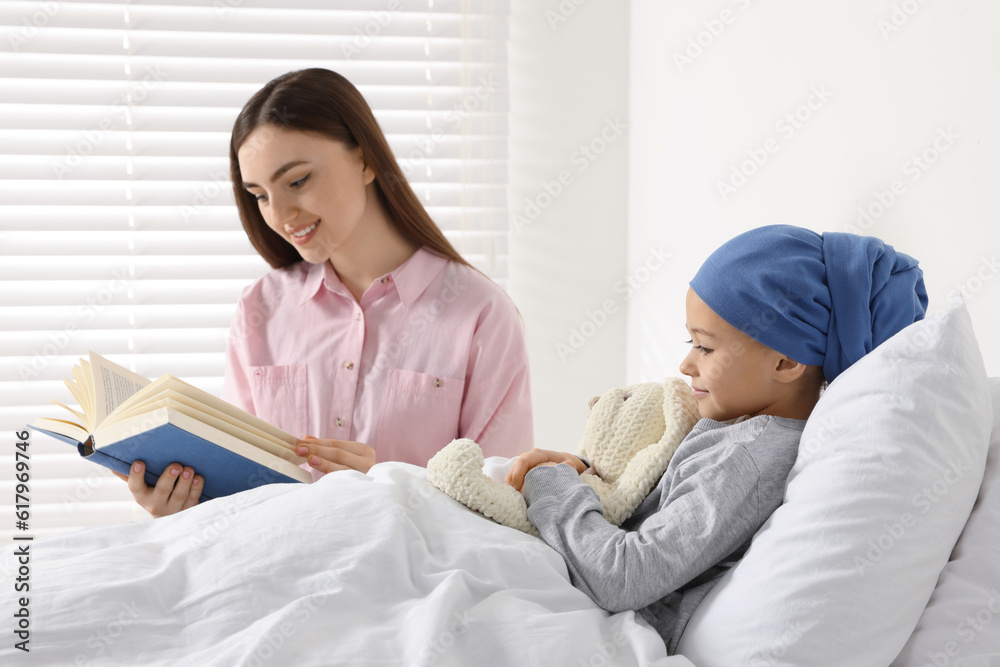 Childhood cancer. Mother reading book to daughter in hospital Childhood cancer. Mother reading book to daughter in hospital