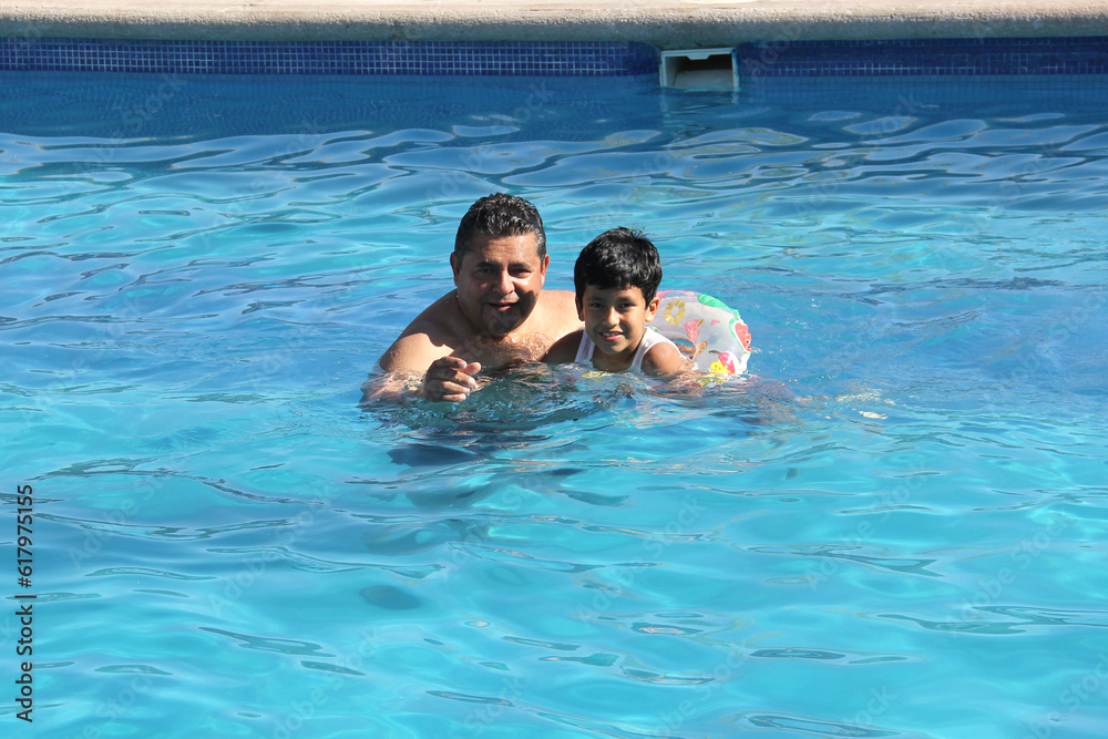 Divorced single dad and 9-year-old black-haired Latino son swim in pool together spend quality family time on summer vacation