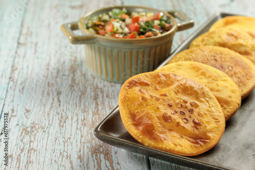 Sopaipillas of pumpkin or squash in rectangular plate on wooden table and bowl with pebre with copy space for typical chilean food concept photo