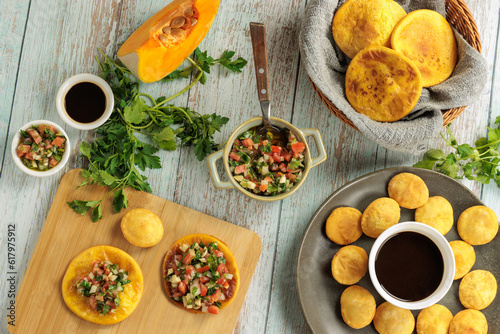 Sopaipillas still life with pumpkin or squash, parsley. in round dish on wooden table, bowls with pebre, chancaca and wooden spoon. aerial view. Typical Chilean food concept