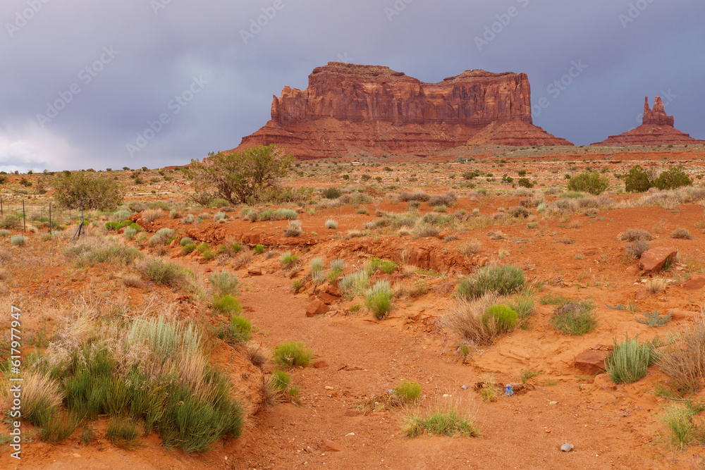 Sandstone formation in monument valley behind a dry creek bed and low lying vegetation