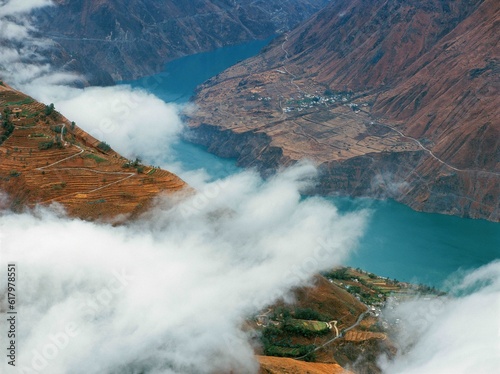 Turquoise colored river bends around mountains surrounded by clouds