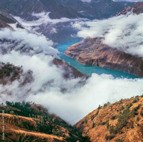 Turquoise colored river bends around mountains surrounded by clouds