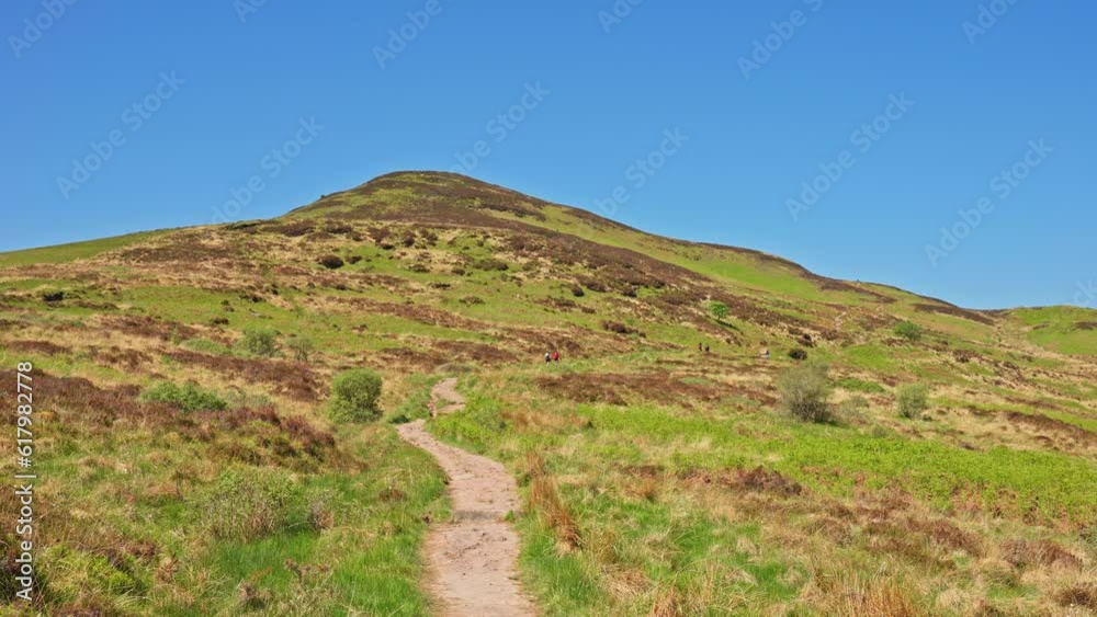 Traveling on a path towards Conic Hill with vibrant blue skies and lush spring grassy fields, Scotland Traveling on a path towards Conic Hill with vibrant blue skies and lush spring grassy fields, Scotland