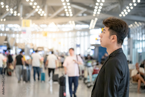 Asian Businessman passenger standing in airport terminal or transportation building with crowded people in the background. Business travel concept