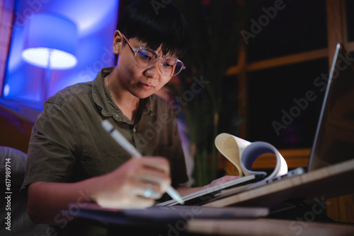 Asian business women freelance working hard by using laptop computer, tablet, and document paper overtime in living room at house. Night overload entrepreneur job with online remotely work at home