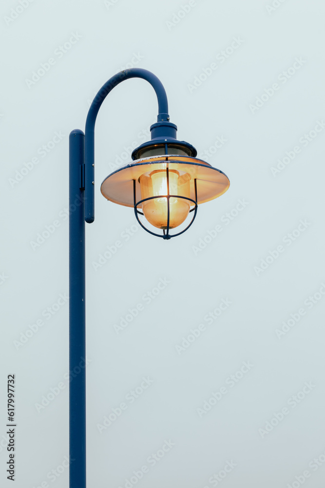 vue sur la tête d'un lampadaire en métal bleu avec la lumière allumée derrière un grillage