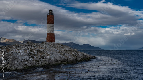An ancient lighthouse stands on a rocky island in the Beagle Channel. A red-and-white striped tower against a  blue sky and clouds. Argentina. The world's southernmost lighthouse Les Eclaireurs © Вера 