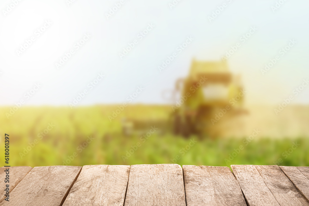 Fototapeta premium Empty wooden table in green field with combine harvester